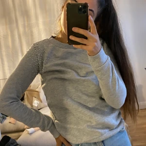 Grå tröja med pärlor. - En grå tröja som jag knappt använt. Med fina pärlor på båda axlarna.