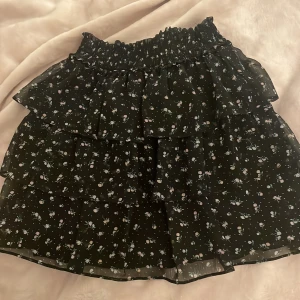 Volangkjol - Somrig volangkjol från H&M. Svart kjol med små blommor på. Nästan aldrig använd och ser ny ut. Storlek xs.