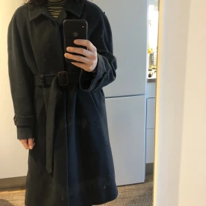 Ullkappa - Lång mörkgrön unisex kappa i ullblandning köpt secondhand. Kan användas med eller utan skärp beroende på look.  Jag är storlek 38/M så sitter oversized på mig, gissar att den är storlek L/42. Säljes då ej kommer till användning. 