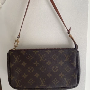 Louis Vuitton pochette - Louis Vuitton pochette väska i bra skick. Använd ganska mycket och har ingen repa eller liknande. Dock är lädret slitet vid läderbandet, vilket framkommer på en bild. Nypris ca 8000 kr  Mått 24x14x4