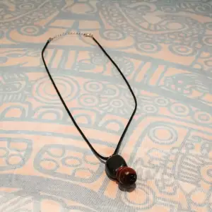 Handgjort (av mig) halsband med ett hänge som består av sten- och träpärlor. Halsbandet har en klassisk låsmekanism i nacken. 🤎
