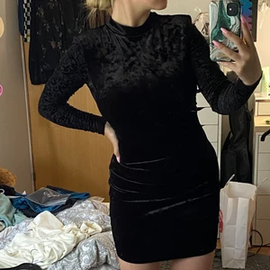 Svart mocka klänning - En svart klänning med mocka tyg och öppning i ryggen. Ärmarna är i ett tunnare mocka tyg och i mönster. Öppning i ryggen. 