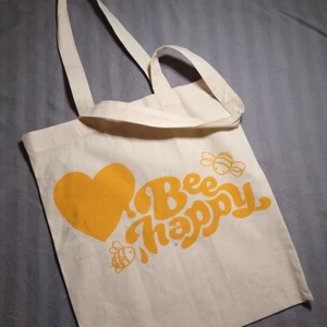 Väska  - En beige tote väska med texten "bee happy", ett gult hjärta och några bin runt om. Inte använts någon gång. Går att ha den som bad väska, en dator får plats eller det som känns bra😊 