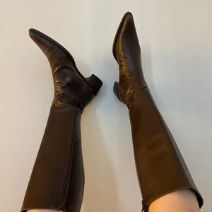 Knähöga bruna stövlar, cowboy - De perfekta höststövlarna med jättefin spetsig tå! De är mörkbruna skinnstövlar som går till strax under knäna på mig som är 168, lite rymligare upptill så passar även de med något större vader. Nypris 350 (second hand så några smååå skavanker)