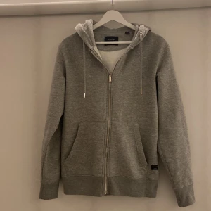 J&J zip up hoodie grå strl M  - Jack and Jones zip up hoodie strl M. Använd vid vissa tillfällen men är i övrigt i mycket bra skick. Säljer då jag ej tycker plaggets passform passar mig lika bra längre. Nypris: 400kr