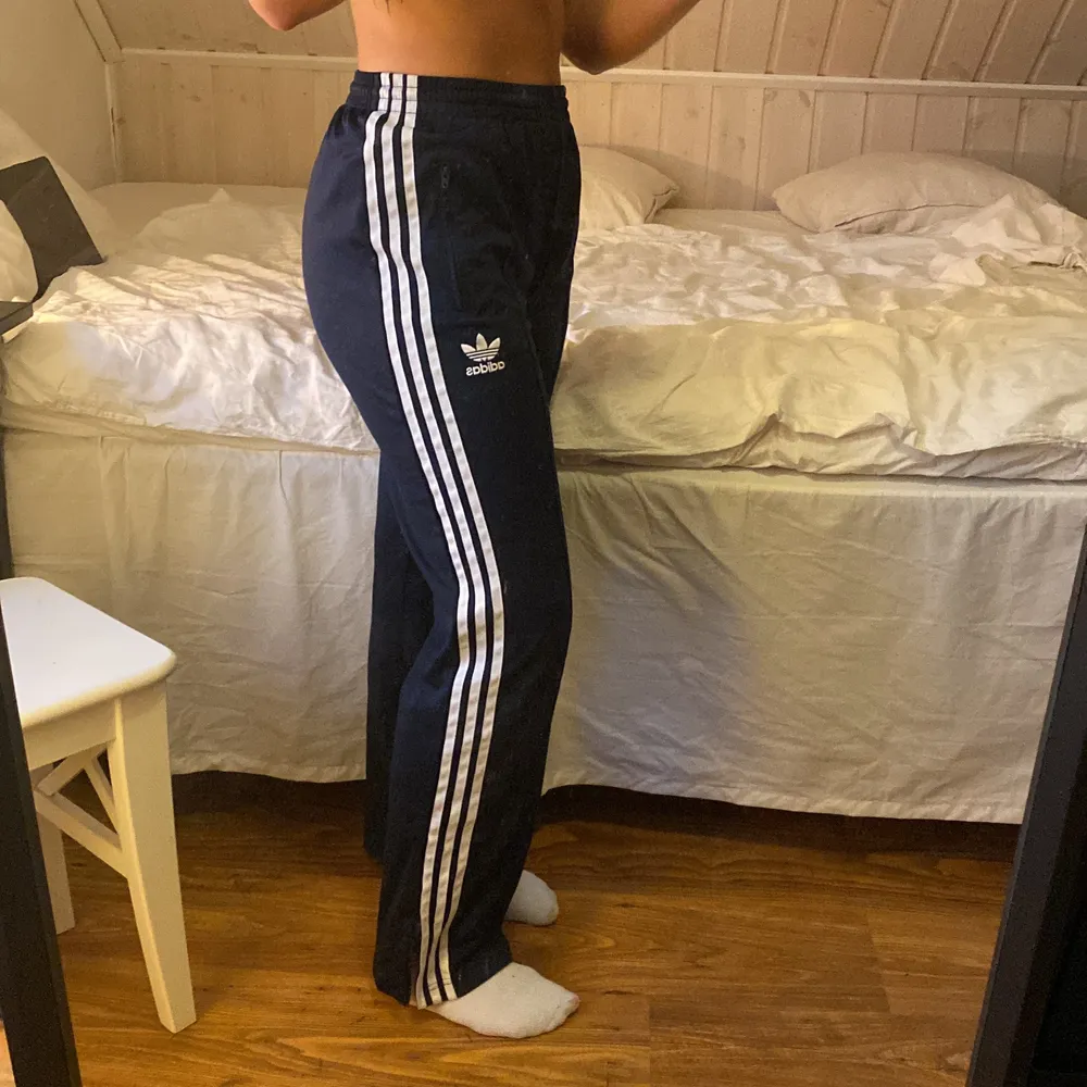 Raka mörkblåa adidasbyxor med vita ränder. 100 polyester. I bra skick med dragkedja både för fickor och nere i byxbenet. Passar XS lösare eller S tajtare (som mig på bilden). Nypris 599kr🌻  (Köparen står för frakt) . Jeans & Byxor.