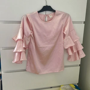 Rosa fest tröja  - Rosa fest tröja, blankt tyg, volanger armar, använd 1 gång för några årsen, legat ett tag i garderoben. Inga anmärkningar 