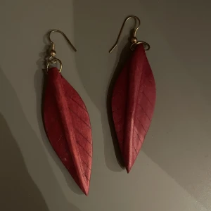 Röda öronhängen  - Röda öronhängen formade som en fjäder. Väldigt unika då dom är i trä! Fint skick🤩