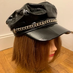 Lack hatt med kedja - Snygg skepparhatt i lack material och dekorativ silverskedja framtill. Aldrig använd, liten för mitt stora huvud. Den är i normal storlek och passar nog de flesta. Med snörning inuti som kan dras åt och krympa den. Fin kvalitet. Gratis vid köp av annat