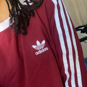 Röd adidas tröja - Denna vinröda långärmde Adidas tröja är har varit använd endast ett par gånger. Tröjan har ett värde på 330 kr då den är äkta men den säljs för 120kr! Alltså mer än 50% billigare. Köparen står för frakten.
