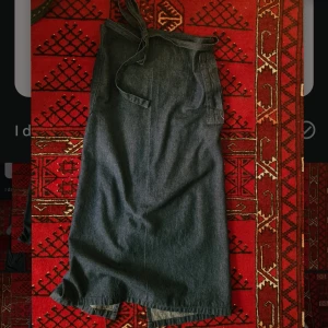 Lång jeanskjol -  Lång omlottkjol i jeans. Jättebra skick. Sista bilden beskriver färg bäst, jag har kjolen på höftbenen typ, min omkrets är 89 cm där. Midjan kan justeras, men kjolen uppskattas till en 38! Tygets längd: 94 cm. Dm för mer info! Inte kollat frakt