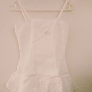 Romantisk vit klänning, 80-tals stil. Strlk: 34/XS-SMALL. Retro. Student. Sommar - Romantisk vit feminin klänning i 1980-tals stil. Fin för sommaren tex midsommar eller skolavslutning/studenten. Har volanger nedtill, reglerbara axelband, samt stretchig resår i sidorna. 34/XS-SMALL. 71 cm lång. Material: Bomull. Felfri. FRAKT TILLKOMMER.
