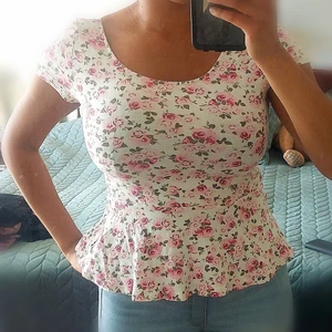 Vit topp med rosa blommönster  - Söt blommig topp med volang nedtill. Åtsittande i midjan så den ger en väldigt fin form. Väl använd Säljer eftersom jag inte längre använder den, men fortfarande fin oxh i bra skick. Storlek M  Öppen för att förhandla pris😊 