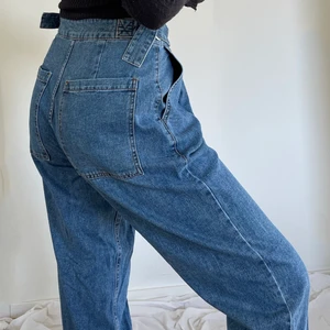 Blåa jeans med fina detaljer - Byxor i baggy design med hög och åtdragbar midja. Med fina silver ringar i midjan och stora fyrkantigt formade fickor får jeansen en speciel+unik stil. Extremt sköna och ej använda då byxorna inte passade med resten av min garderob. Skriv för fler bilder❤️