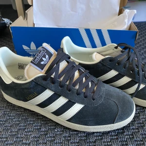 Adidas Gazelle sneakers - Säljer dessa snygga skor från adidas då de tyvärr var för små. Använda en gång! Nypris 1199kr Färg: carbon/off white Storlek: 38 1/3 Original box + vita skosnören medföljer