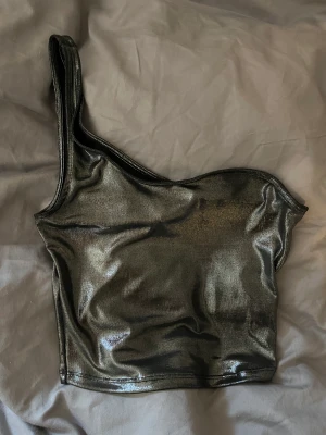 Cool festtopp - Skitsnygg festtopp i glittrigt tyg, one shoulder. Knappt använd, från hm strl xs. Säljer för 60kr.
