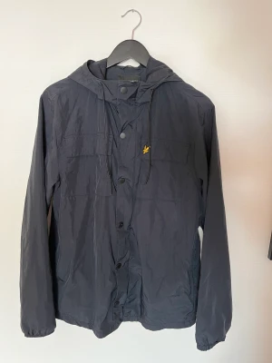 Lyle & Scott vårjacka - Marinblå Lyle and Scott vår/höst-jacka. Mycket bra skick. Har dock en liten skada som syddes ihop (se bild) men syns inte alls då den sitter på undersidan av armen. Nypris ca 1000 kr