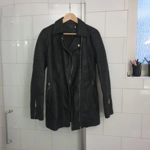 Skinnjacka - Längre jacka i skinnimitation.  Aldrig använts. Osäker på storleken står att det är storlek 3.  Strechig.
