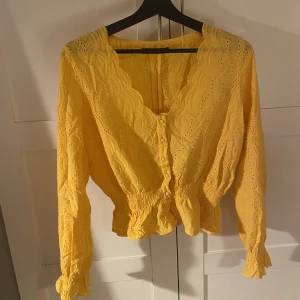 Gul blus - Gul somrig blus från Bikbok, med knappar framtill, v-ringad, volanger i ärmarna och nedtill i midjan, sytt mönster. Nypris 349kr. Frakt tillkommer!!!!
