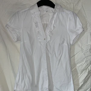 Vit skortärmad skjorta - Så söt och fin vit skjorta! Har en volang vid kragen och den är fint figursyddd! 