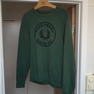 Grön sweatshirt från Fred Perry  - Grön Fred Perry sweatshirt i M. Bra skick, men har en liten plast bit på ena ärmen (syns o högra hörnet på andra bilden)