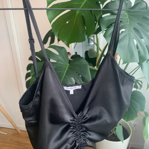 Svart topp från chiquelle strl L - Skitsnygg svart silkestopp från Chiquelle! Storlek L på denna, med justerbara axelband. Man kan även dra åt i snörena mitt på för att forma den som man själv vill. Säljer för 50kr