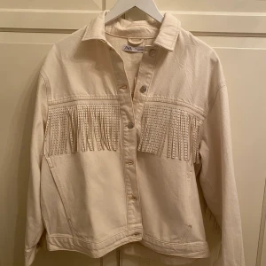 Jeans jacka - Säljer min jätte fina jeans jacka från Zara. Den har fransar på ryggen som även går ner över ärmarna, den är i en beige jeans färg, har två fickor. Den är aldrig använd, därför säljer jag den. I storlek M