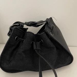 Minihandväska, svart - Väskan har inte används och är i ett mycket gott skick. Väskan kan stylas med varje outfit och är praktiskt att ta med sig överallt. Väskan är dessutom justerbar som gör att den kan anpassas sig efter ditt val av storlek