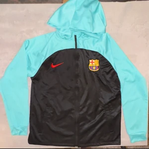 FC Barcelona träningsset  - Säljer ett snyggt FC Barcelona träningsset frăn Nike - jacka och matchande byxa і toppskick! Jackan har svart front med röda Nike-loggan och klubbmärket, samt turkosa ärmar och luva. Byxorna är svarta med mätt: • Midja: 30 cm • Längd: 95 cm Perfekt för dig som älskar Barca eller bara vill ha ett bekvämt och sportigt set till vardag eller träning. V Nike V Bra skick • Unisex passform