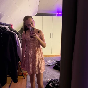 Blommig offshoulder kortklänning - Superfin kortklänning med offshoulder och smock upptill. Klänningen är orange/aprikos med vitt blommigt mönster och har en flowy kjol. Perfekt för varma dagar och har en söt, ungdomlig vibe. Materialet känns lätt och bekvämt mot huden.