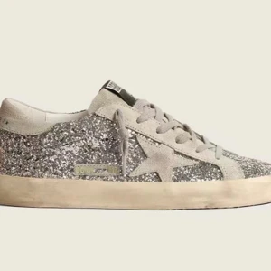 Golden Goose Super-Star glitter sneakers - Snygga sneakers från Golden Goose med silverglittrigt tyg och en ikonisk stjärna i mocka på sidan. Skon har snörning och en platt sula i beige ton. Perfekt för dig som vill sticka ut med lite extra bling i vardagen. Köptes från Vinted för 3100kr, känns lite för dyra att ha på sig 😍