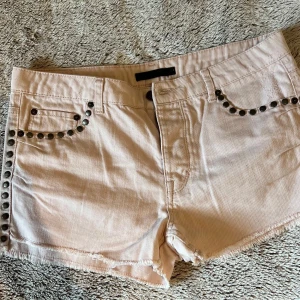 Ljusrosa jeansshorts med nitar Gina Tricot - Rosa shorts med nitar längs fickorna och sidorna. Shortsen har en rå kant nedtill och två fickor bak. Storlek 38