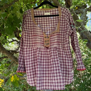 Rutig blus från Odd Molly, storlek 3 - Superfin rutig blus från Odd Molly i vinröda och vita toner. Blusen har lång ärm med volangkant, v-ringning med spetsdetaljer och dekorativa knappar framtill. Broderade detaljer och mjukt bomullsmaterial gör den extra comfy och snygg. Storlek 3 som enligt deras storleksguide motsvarar en storlek L.  Mycket fint skick, jag hittar inga synliga anmärkningar eller defekter.