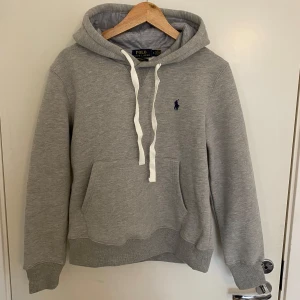 Polo Ralph Lauren hoodie - Säljer en stilren grå hoodie från Polo Ralph Lauren med klassisk logga på bröstet. Tröjan är i mycket bra skick och säljs för att den är för liten för mig! Hör av dig vid minsta fundering!