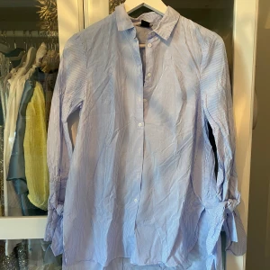 Blårandig skjortklänning med knyt vid ärmar - Snygg blårandig längre skjorta/tunika med klassisk krage och knappar framtill. Långärmad modell med coola knyt-detaljer vid ärmsluten. Perfekt för dig som gillar en relaxed men ändå stilren look💝💝 Endast använd en gång!