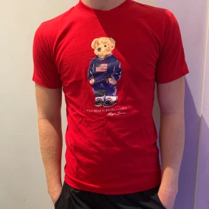 Polo bear t-shirt  - Riktigt snygg röd t-shirt från Ralph Lauren med Polo Bear-tryck på bröstet. Klassisk rund hals och korta ärmar. T-shirten är i mjuk bomull och har Polo-logga tryckt i vitt på ryggen. Perfekt för dig som gillar streetwear med en twist. Neck tagen är bortklippt och därav priset. Modellen är 180cm och väger 73kg