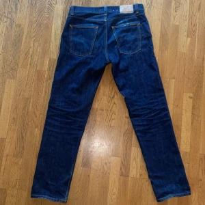 Mörkblå jeans från Nudie Jeans - Snygga mörkblå jeans från Nudie Jeans med klassisk femficksdesign och raka ben. Jeansen har kontrastsömmar, läderpatch bak i midjan och är tillverkade i slitstarkt denim av bomull. Perfekta för dig som gillar en clean och tidlös look.