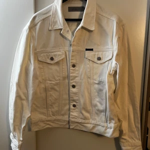 Vit jeansjacka från Calvin Klein Jeans - Snygg vit jeansjacka från Calvin Klein Jeans (som är knappt använd) i klassisk modell med knappar framtill och två bröstfickor med lock. Jackan har en rak passform och är tillverkad i bomull. 