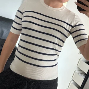 Short sleeve sweater - Snygg vit topp med marinblå horisontella ränder och rund hals. Modellen är figurnära med korta ärmar och bred ribbad mudd nedtill. Perfekt för en stilren och klassisk look. Materialet känns mjukt och stretchigt.