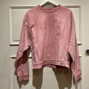 Rosa sweatshirt från Levi's i bomull - Säljer en chill rosa sweatshirt från Levi's i storlek S. Tröjan har broderad logga framtill, ribbade muddar och rund hals. Mjuk bomullskvalitet och loose passform, perfekt för sköna dagar. Färgen är ljusrosa och designen är enkel men snygg.
