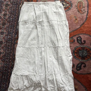 Vit långkjol från Brandy Melville - Supersöt vit långkjol från Brandy Melville med volangdetaljer och elastisk midja. Kjolen har flera lager och är gjord i mjukt bomullstyg som ger en flowy och chill vibe. Perfekt att styla med sneakers eller sandaler för en fräsch look.