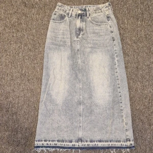 Ljusblå lång jeanskjol med rå kant - Säljer en ljusblå lång jeanskjol med klassisk femficksdesign och hög midja. Kjolen har en rak siluett och rå, fransad kant längst ner för en cool vibe. Perfekt att matcha med sneakers eller boots för en avslappnad look. Använd bara en gång. 