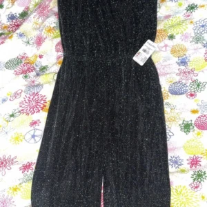 Glittrig svart långklänning - Snygg svart långklänning med glittriga detaljer som ger en festlig vibe. Klänningen har en rak siluett och resår i midjan för skön passform. Materialet är mjukt och skimrande, perfekt för dig som gillar att sticka ut. Slits framtill för extra edge.