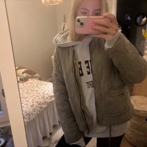 Beige quiltad jacka med dragkedja - Säljer en beige quiltad jacka med dragkedja framtill och två fickor. Jackan har en loose passform och är tillverkad i mjuk manchester med vågigt quiltat mönster. Perfekt att slänga på över hoodien för en chill look.