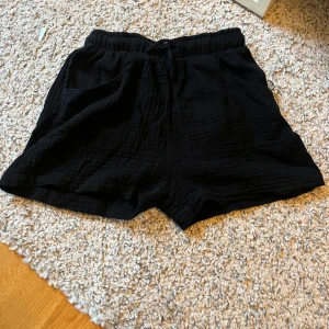 Svarta shorts från 157 med snörning - Svarta shorts från 157 i mjukt, strukturerat bomullstyg. De har elastisk midja med snörning och två sidofickor. Passformen är loose och de är perfekta för chill dagar under sommaren. Enkla att matcha med en t-shirt eller hoodie.