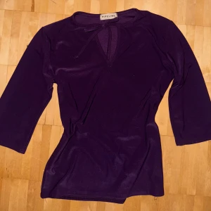 Lila blus med knyt  - Säljer en snygg unik lila blus från Pipeline med trekvartsärm och v-ringning med knytband vid halsen. Toppens material har en lätt glansig finish som ger en cool look.