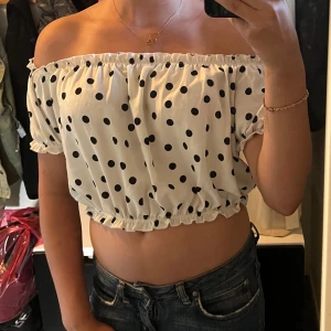Prickig offshoulder croppad topp XOXO - Superfin vit offshoulder croppad topp från XOXO friends med svarta prickar. Toppens resår vid axlar, ärmslut och midja ger en snygg puffig look. Perfekt till jeans eller kjol för en trendig vibe.