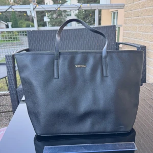 Ny Svart väska / bag - Helt ny stor och stilren svart hand /axel väska med två rejäla handtag. Väskan har en enkel, fyrkantig form och är tillverkad i slätt syntetmaterial. Insidan är ljusbeige med flera fack och dragkedja för smidig organisering. Perfekt för dig som vill ha plats för allt. Kan hämtas på Hägerstensåsen i Stockholm. 