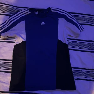 Blå Adidas t-shirt med vita ränder - Snygg blå t-shirt från Adidas med klassiska vita ränder längs axlarna och logga på bröstet. använd 1-2 gånger, sedan har den varit liten för mig.T-shirten har korta ärmar och är gjord i mjukt och lätt bomullsmaterial, kan skicka fler bilde om ni behöver och de bara fråga på om några frågor finns.