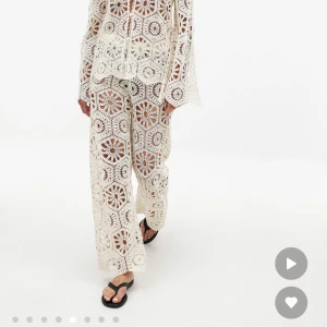 Vita virkade byxor med blommönster - Säljer ett par vita virkade byxor med blommönster och breda ben. Byxorna har en transparent look och är gjorda i ett stickat material med coola geometriska och blommiga detaljer. Perfekt för dig som vill sticka ut med en unik och bohemisk stil. Endast testat men kunde inte lämna tillbaka då det hade gått för många dagar